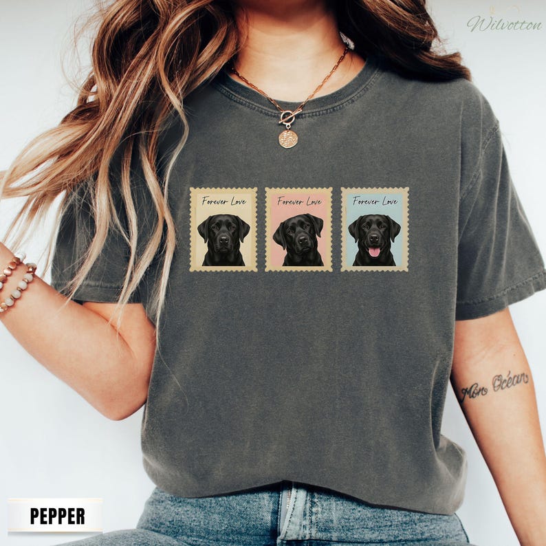 May include: Dark grey t-shirt with three postage stamp designs. Each stamp features a black Labrador Retriever portrait and the text "Forever Love". The stamps have beige backgrounds with pink and blue accents. The shirt is made of a soft material.