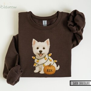 May include: Dark chocolate brown sweatshirt featuring a white dog with a candy corn light strand and a pumpkin with the name "REX". The sweatshirt has long sleeves and a crew neck. The text "DARK CHOCOLATE" is in a black rectangle.