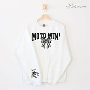 May include: White sweatshirt with the text "MOTO MIMI" in black block letters, a checkered bow graphic, and a motorcycle graphic with the name "Jaxson" and the number "45".