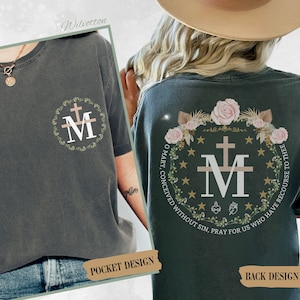 May include: A dark green t-shirt with a pocket on the left side featuring a stylized image of the Miraculous Medal. The back of the shirt features a larger image of the Miraculous Medal surrounded by a wreath of flowers and stars. The text "O Mary, conceived without sin, pray for us who have recourse to thee" is printed around the medal.