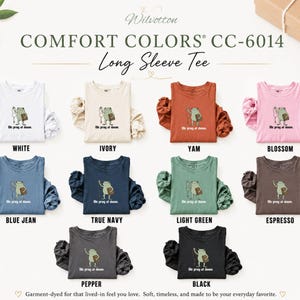 May include: A collection of Comfort Colors CC-6014 long sleeve tees in ten colors: white, ivory, yam, blossom, blue jean, true navy, light green, espresso, pepper, and black. Each shirt features a graphic of a frog with the text We pray at dawn.