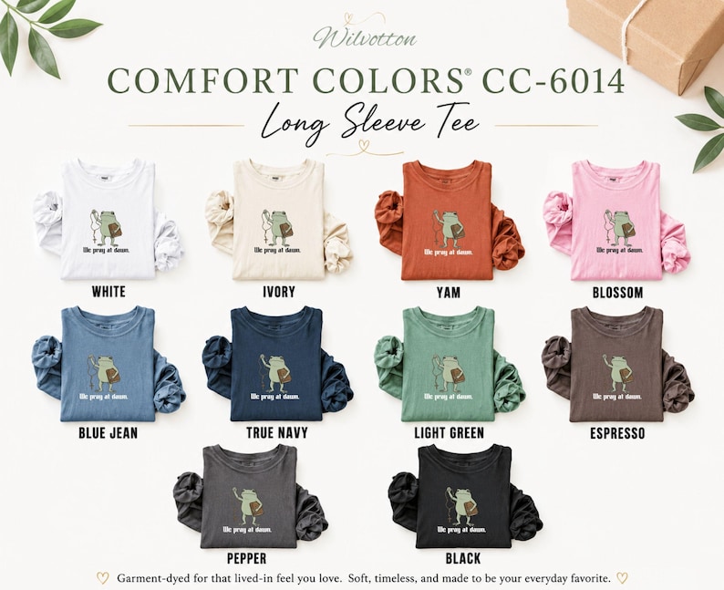 May include: A collection of Comfort Colors CC-6014 long sleeve tees in ten colors: white, ivory, yam, blossom, blue jean, true navy, light green, espresso, pepper, and black. Each shirt features a graphic of a frog with the text We pray at dawn.