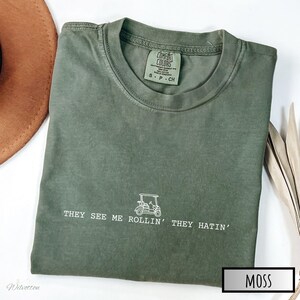 May include: A green t-shirt with the text "THEY SEE ME ROLLIN' THEY HATIN'" and a small graphic of a golf cart. The shirt has a tag that says "COMFORT COLORS" and "S.P. - CH".