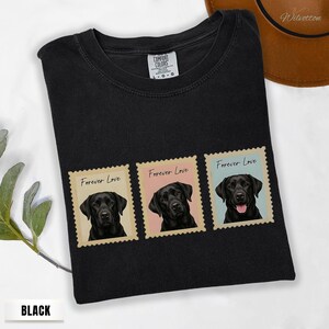 May include: Black t-shirt with three postage stamp designs, each showing a black Labrador Retriever. The stamps read "Forever Love" and have pastel backgrounds. The shirt is from "Comfort Colors".