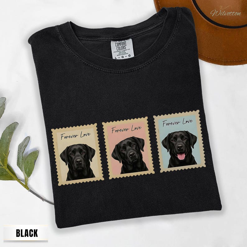 May include: Black t-shirt with three postage stamp designs, each showing a black Labrador Retriever. The stamps read "Forever Love" and have pastel backgrounds. The shirt is from "Comfort Colors".