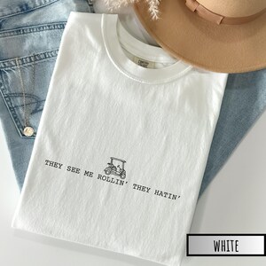 May include: White t-shirt with a black graphic of a golf cart and the text "They see me rollin' they hatin'".