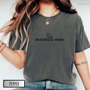 May include: A dark grey t-shirt with a small dachshund silhouette and the text "dachshund mama" printed on the front.