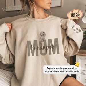 May include: Beige sweatshirt with a brown graphic of a Cockapoo dog and the word "MOM" in brown text. The text "YOUR PET NAME HERE" is in a white speech bubble.