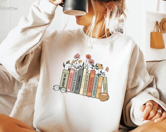 May include: A white sweatshirt with a graphic of a stack of books with titles like "Auditing 101", "Profit & Loss", and "Tax Planning". The books are surrounded by small pink and green flowers.