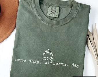May include: A moss green t-shirt with a white graphic of a ship and the text "same ship, different day".