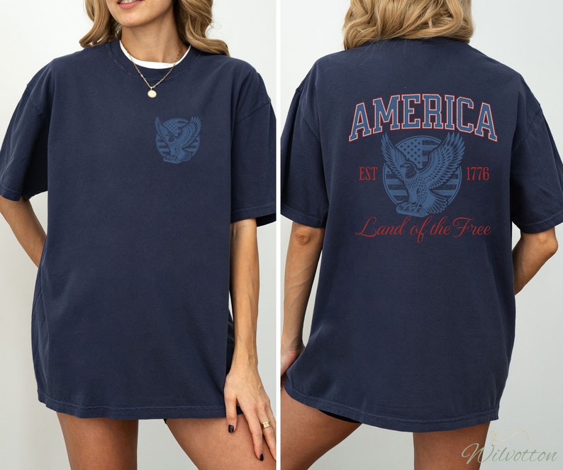 Puede incluir: Una camiseta azul marino con un gr&aacute;fico de un &aacute;guila y las palabras "AMERICA EST 1776 Land of the Free" impresas en la espalda.