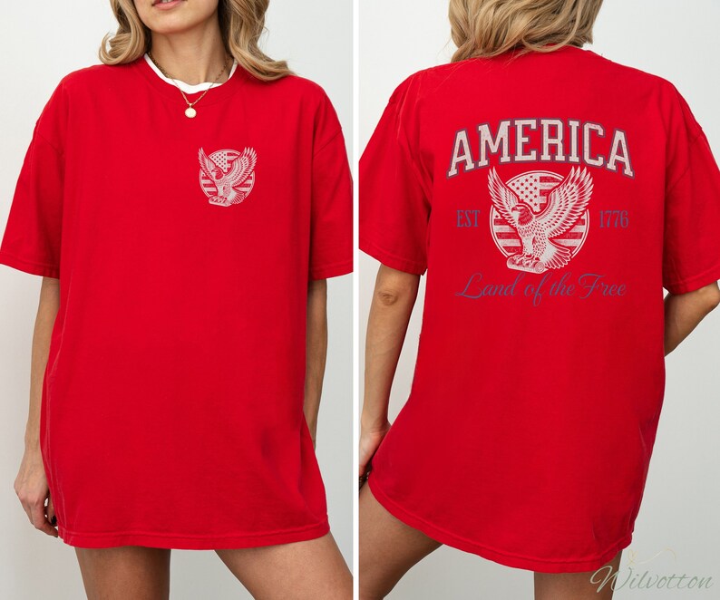 Puede incluir: Camiseta roja de gran tama&ntilde;o con un gr&aacute;fico de un &aacute;guila y el texto "AMERICA EST. 1776 Land of the Free" en la parte posterior.