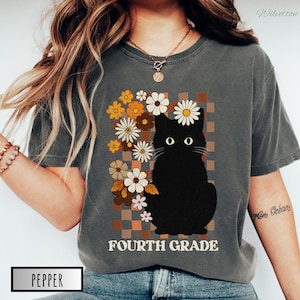 May include: Dark gray t-shirt featuring a black cat illustration with daisy and floral accents. The words "FOURTH GRADE" are printed below the cat. The shirt has a vintage, retro style.