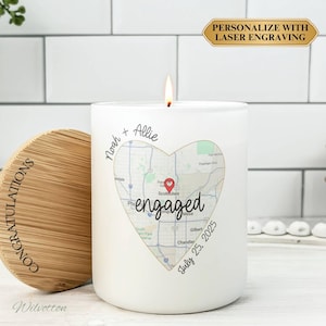May include: A white candle with a heart-shaped map design and the word "engaged". The candle has the names "Noah + Allie" and the date "July 25, 2025". A wooden lid with the word "CONGRATULATIONS" is next to the candle.