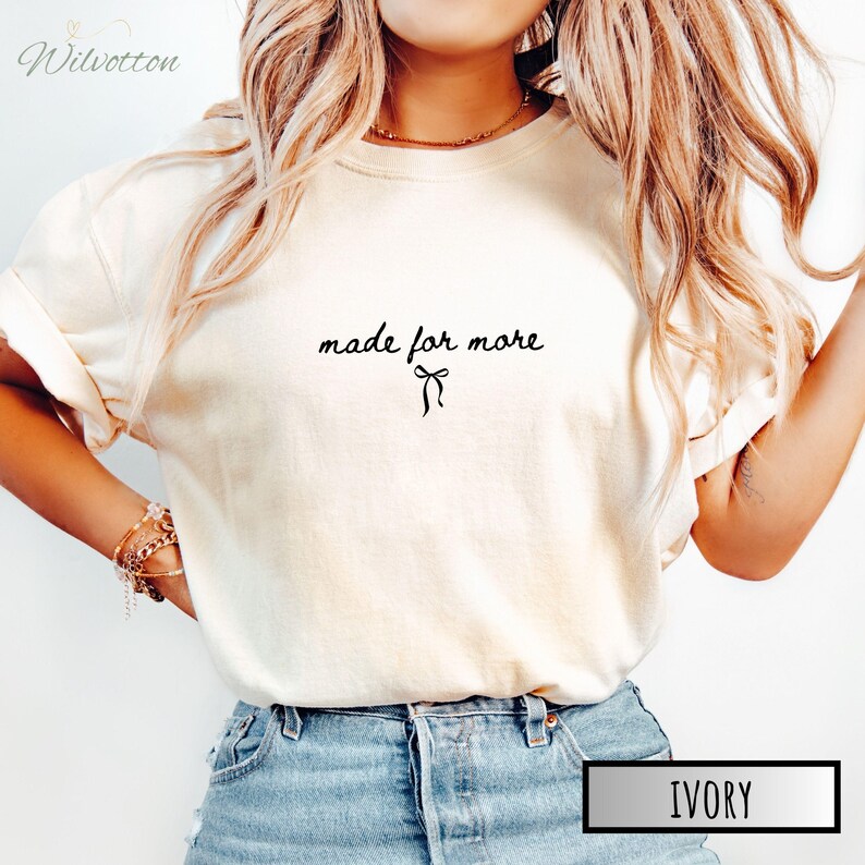 Puede incluir: Camiseta color marfil con la frase "made for more" en una escritura delicada, acompa&ntilde;ada de un peque&ntilde;o lazo. La camiseta es de tono neutro, adecuada para varios conjuntos. La palabra "IVORY" se muestra en un recuadro.