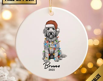 May include: A white ceramic Christmas ornament featuring a dog wearing a Santa hat and wrapped in colorful Christmas lights. The dog's name, "Bruno", and the year "2025" are written below the dog. A gold ribbon is attached for hanging.