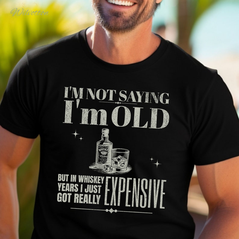 Puede incluir: Una camiseta negra con un gr&aacute;fico blanco que dice "No estoy diciendo que soy viejo, pero en a&ntilde;os de whisky me he vuelto realmente caro". El gr&aacute;fico tambi&eacute;n incluye una botella de whisky y un vaso de whisky con hielo.