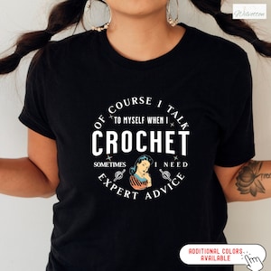 May include: Black t-shirt with a white circle graphic that says "Of course I talk to myself when I crochet. Sometimes I need expert advice."