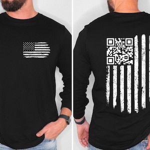 May include: Black long-sleeve shirt with a distressed American flag graphic on the front and back. The front features a small flag, while the back displays a QR code within the flag design. The shirt is made of a soft material.