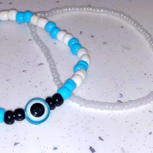 Puede incluir: Dos pulseras de cuentas. Una pulsera presenta cuentas blancas y turquesas alternas. La otra pulsera está hecha de pequeñas cuentas transparentes. Una tercera pulsera tiene un dije de ojo azul con cuentas negras.