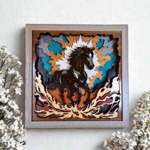 Puede incluir: Un cuadro decorativo cuadrado de madera con un diseño de capas recortadas que muestra un caballo marrón oscuro galopando entre llamas estilizadas. La obra utiliza tonos azules, grises y naranjas, enmarcada en un marco de madera clara.