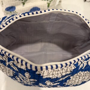 May include: A blue and white floral patterned cosmetic bag with a white zipper and a gray interior. The bag is open, revealing the inside. Another bag with a similar floral pattern is visible in the background.