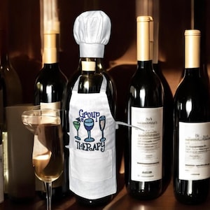 May include: A white apron with the text "Group Therapy" and a graphic of three wine glasses. The apron is worn on a wine bottle with a white chef's hat.