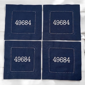 May include: Four navy blue linen napkins with white embroidered stitching around the edges and the number 49684 in white embroidery in the center of each napkin.
