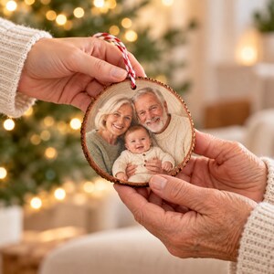 Geschenkübergabe des Foto von Oma, Opa und Enkelkind-Anhängers an eine frischgebackene Oma, mit glaubwürdigem Handmaßstab und sichtbarem Foto von Oma, Opa und Enkelkind.