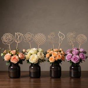 May include: Four dark brown ceramic vases filled with colorful roses and greenery, each topped with a wooden flower cutout on a stick. The flowers are in shades of peach, white, orange, and purple.