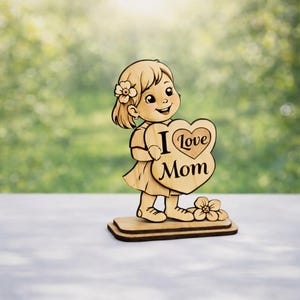 May include: Wooden figurine of a smiling girl holding a heart-shaped sign that reads "I Love Mom." The figurine is light brown with a flower in her hair and stands on a rectangular base. A flower is at her feet.