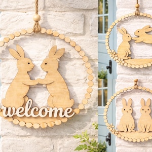Peut inclure: Couronne de Pâques en bois avec deux lapins se tenant la main et le mot "welcome". La couronne ronde a une bordure perlée et une corde de jute pour la suspension. D'autres couronnes avec des motifs de lapins sont également présentées.