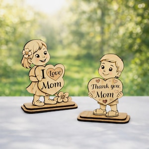 Puede incluir: Dos figuras de madera de niños sosteniendo carteles en forma de corazón. Uno dice "I love Mom" y el otro "Thank you, Mom". Ambos están sobre bases rectangulares, con un acabado de madera natural. Una flor está al lado de la niña.