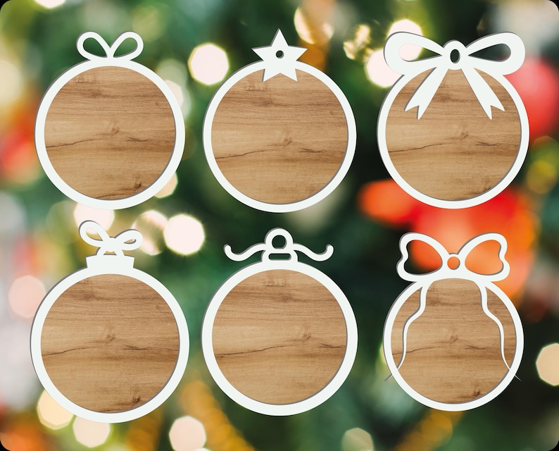 Puede incluir: Seis adornos navide&ntilde;os con marco blanco y centros con aspecto de madera. Cada adorno tiene una parte superior decorativa diferente, incluyendo lazos y una estrella. Los adornos se colocan sobre un fondo borroso de luces y vegetaci&oacute;n navide&ntilde;as.