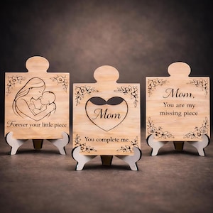 May include: Three wooden puzzle pieces with white stands. The pieces feature engraved designs and text, including a mother and child, a heart with the word "Mom," and the phrase "You are my missing piece." Floral accents adorn the edges.