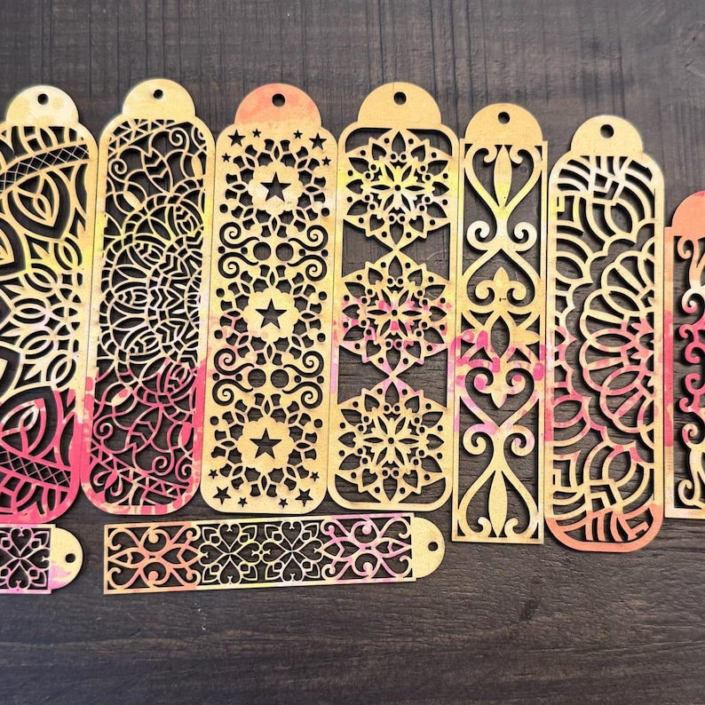 May include: A set of ten laser-cut wooden bookmarks with intricate designs. The bookmarks are in shades of yellow, orange, and pink. Each bookmark features a different pattern, including mandalas, stars, and swirls.