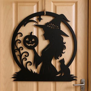 Peut inclure: Décoration d'Halloween en bois noir représentant une silhouette de sorcière tenant une citrouille sculptée. La sorcière porte un chapeau pointu, entourée d'un cadre circulaire avec un chat et une étoile. Suspendu par une corde en jute.