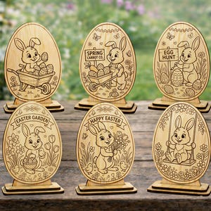 Peut inclure: Décorations en bois en forme d'œufs de Pâques avec des motifs de lapins découpés au laser. Chaque œuf présente une scène différente, avec des lapins, des carottes, des œufs et les textes "Spring Carrot Co.", "Egg Hunt", "Easter Garden", et "Happy Easter".