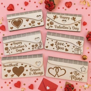 May include: A collection of six wooden Valentine's Day themed gift boxes. Each box features a unique design, including hearts, roses, and phrases like "Happy Valentine's Day," "Love You," and "Be Mine." The boxes are light-colored with dark brown engraved details.