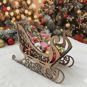 May include: A wooden sleigh filled with wrapped candies and candy canes. The sleigh has decorative snowflake cutouts and is set against a blurred background of Christmas trees and ornaments. A festive holiday decoration.
