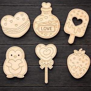 May include: A collection of six wooden cutouts in various shapes: a heart-shaped macaron, a potion bottle with "LOVE" text, an ice cream bar with a heart cutout, a penguin holding a heart, a heart-shaped lollipop, and a strawberry. All are made of light-colored wood.