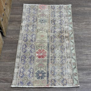 May include: Rectangular, vintage-style rug with a distressed appearance. The rug features a patchwork design with floral and geometric patterns in shades of blue, red, green, and beige. The rug is placed on a dark wood surface.