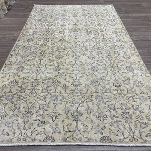 May include: A rectangular, vintage-style rug with an intricate floral pattern in shades of beige, gray, and blue. The rug has a distressed appearance, suggesting it is an antique or a reproduction with a worn look. The design features stylized flowers and vines.