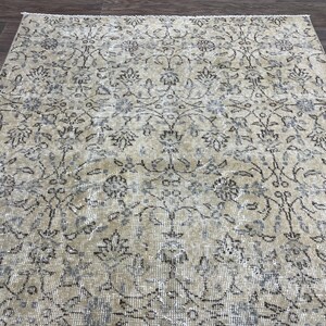 May include: A beige and gray patterned rug with an intricate floral design. The rug has a distressed, vintage look, with faded colors and a detailed pattern. The rug is rectangular and appears to be made of woven material.