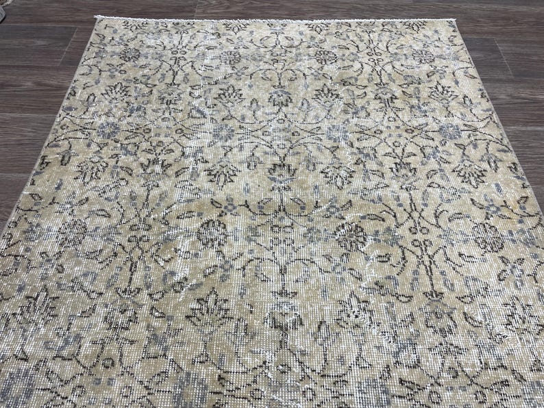 May include: A beige and gray patterned rug with an intricate floral design. The rug has a distressed, vintage look, with faded colors and a detailed pattern. The rug is rectangular and appears to be made of woven material.