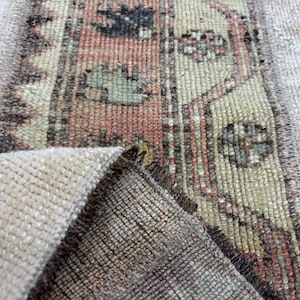 Puede incluir: Primer plano de una sección de una alfombra vintage. La alfombra presenta un fondo beige con un diseño central en tonos rojos, verdes y beige. Los bordes de la alfombra están deshilachados y la textura es visible.