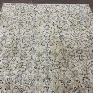 May include: A beige and gray patterned rug with an intricate floral design. The rug has a distressed, vintage look, with faded colors and a detailed pattern of flowers and vines. The rug is rectangular and appears to be made of a woven material.