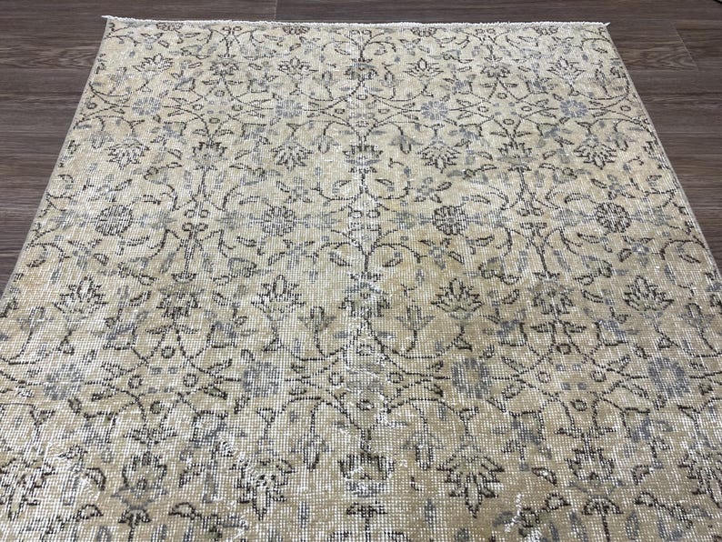 May include: A beige and gray patterned rug with an intricate floral design. The rug has a distressed, vintage look, with faded colors and a detailed pattern of flowers and vines. The rug is rectangular and appears to be made of a woven material.