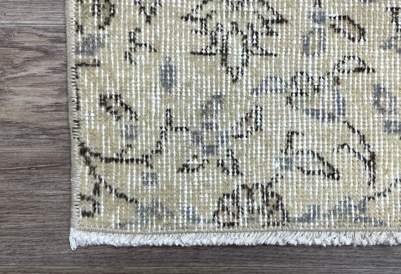 May include: Close-up of a section of a beige and gray patterned rug with a distressed look. The rug has a fringe on the bottom edge and is placed on a wooden surface.