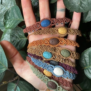 Könnte beinhalten: Ein Stapel von acht Armbändern mit verschiedenen farbigen Lavasteinen und Makramee-Schnur. Die Armbänder sind braun, orange, blau, grün, lila und grau.